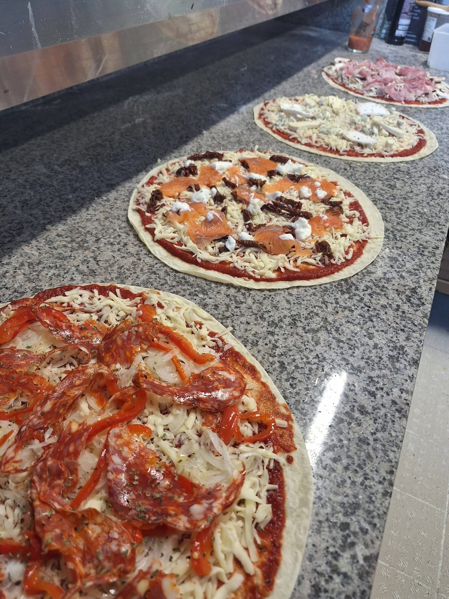 Pizzas garnies alignées sur le plan de travail en granit, prêtes à cuire